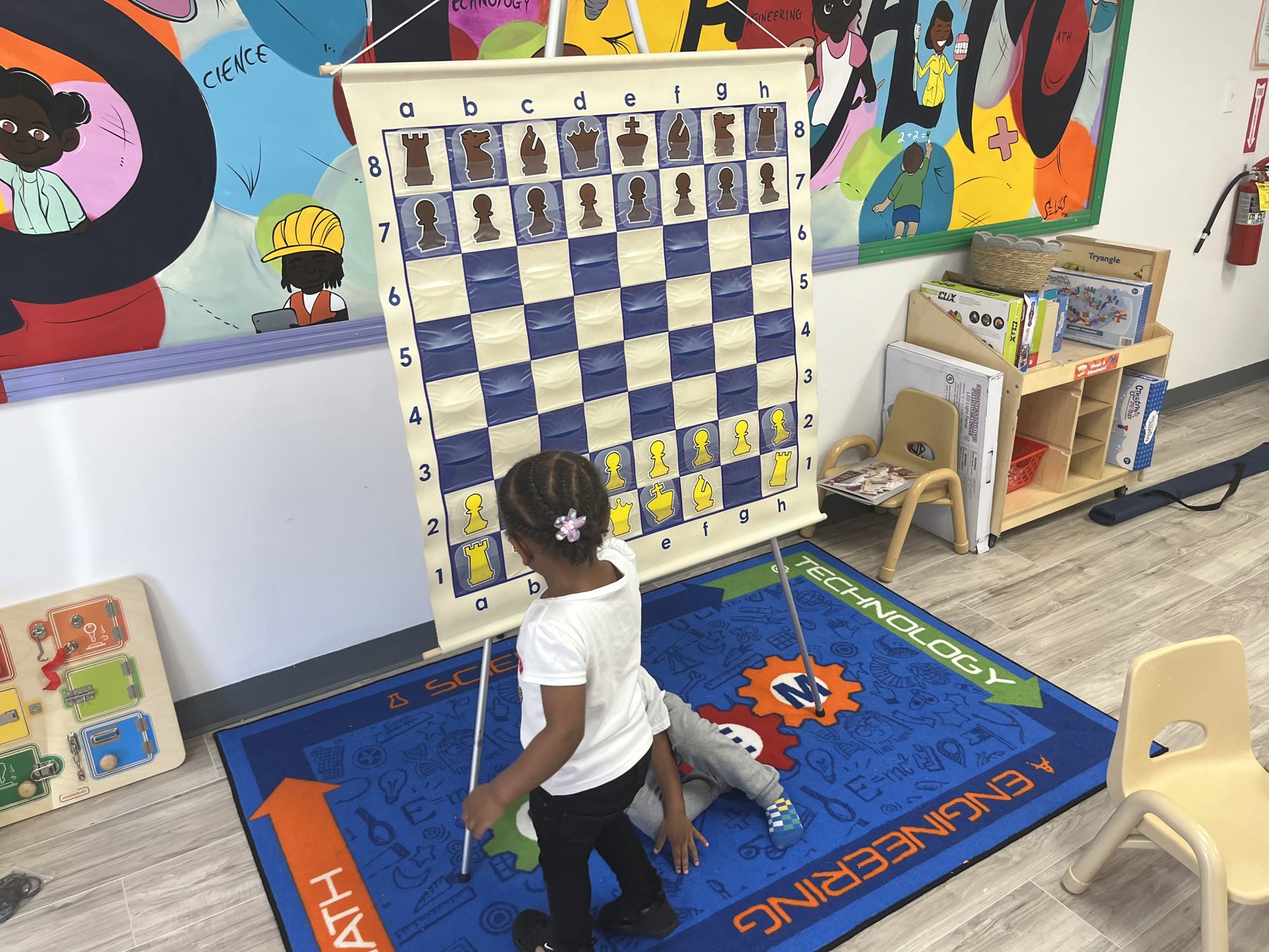 Preschooler moving pieces on a giant wall chess board in the STEAM Innovation Lab